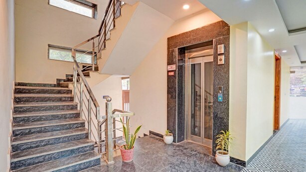 A hotel lobby with a marble staircase, an elevator, and potted plants. - SnapStayz (Noida)