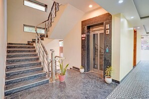 Un hall de hotel con una escalera de mármol, un ascensor y plantas en macetas.