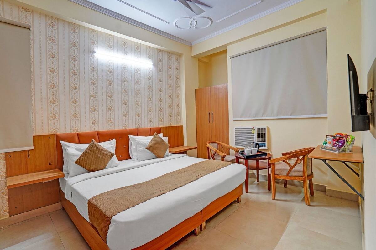 Quarto de hotel com cama, escrivaninha, cadeira, guarda-roupa e janela com persianas.