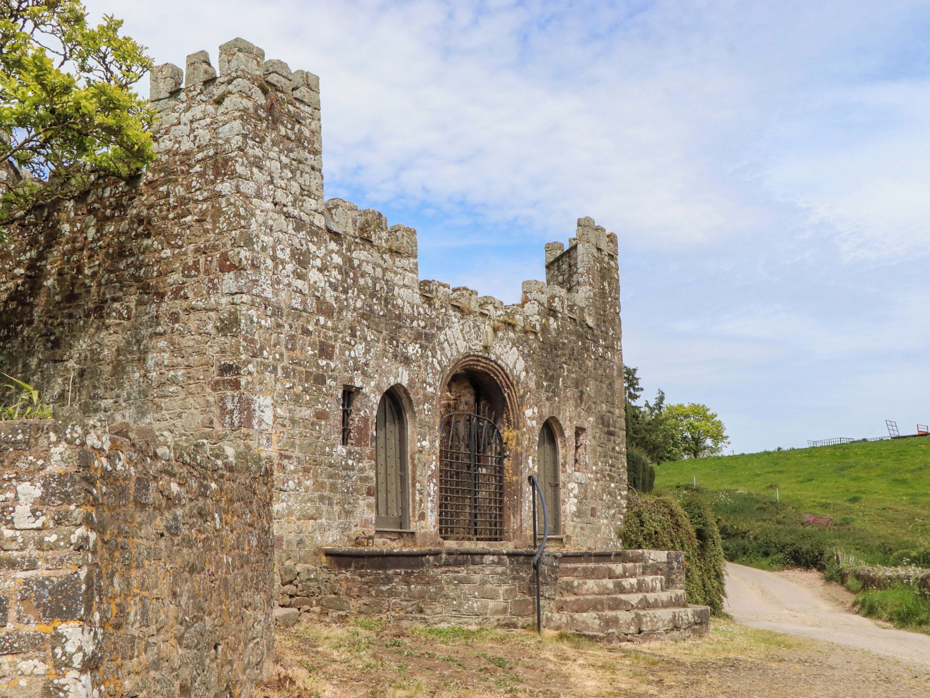 An old stone building with arched windows and a gate, surrounded by a grassy area.