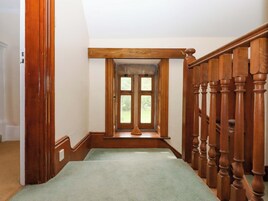Una escalera de madera con alfombra verde, barandilla de madera y una ventana con vistas a follaje.