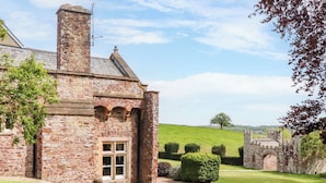 A stone building with a chimney, a window, and a well-maintained lawn. - Dowrich West Wing Apartment (Crediton)