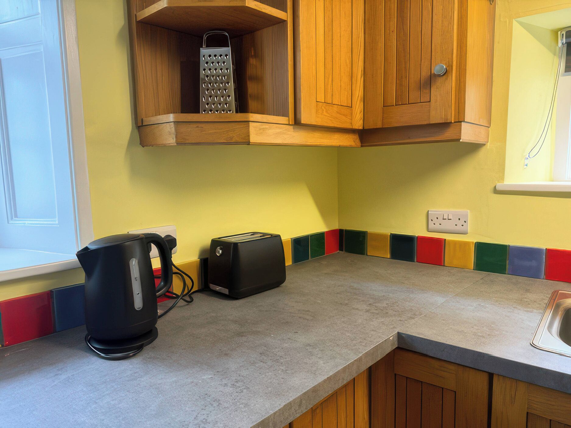 Una cocina con armarios de madera, tetera, tostadora y un protector contra salpicaduras colorido.