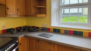 A kitchen with wooden cabinets, a stove, a window with a view, and a colorful backsplash. - Dowrich West Wing Apartment (Crediton)