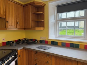 Una cocina con armarios de madera, estufa, ventana con vistas y salpicadero de colores.
