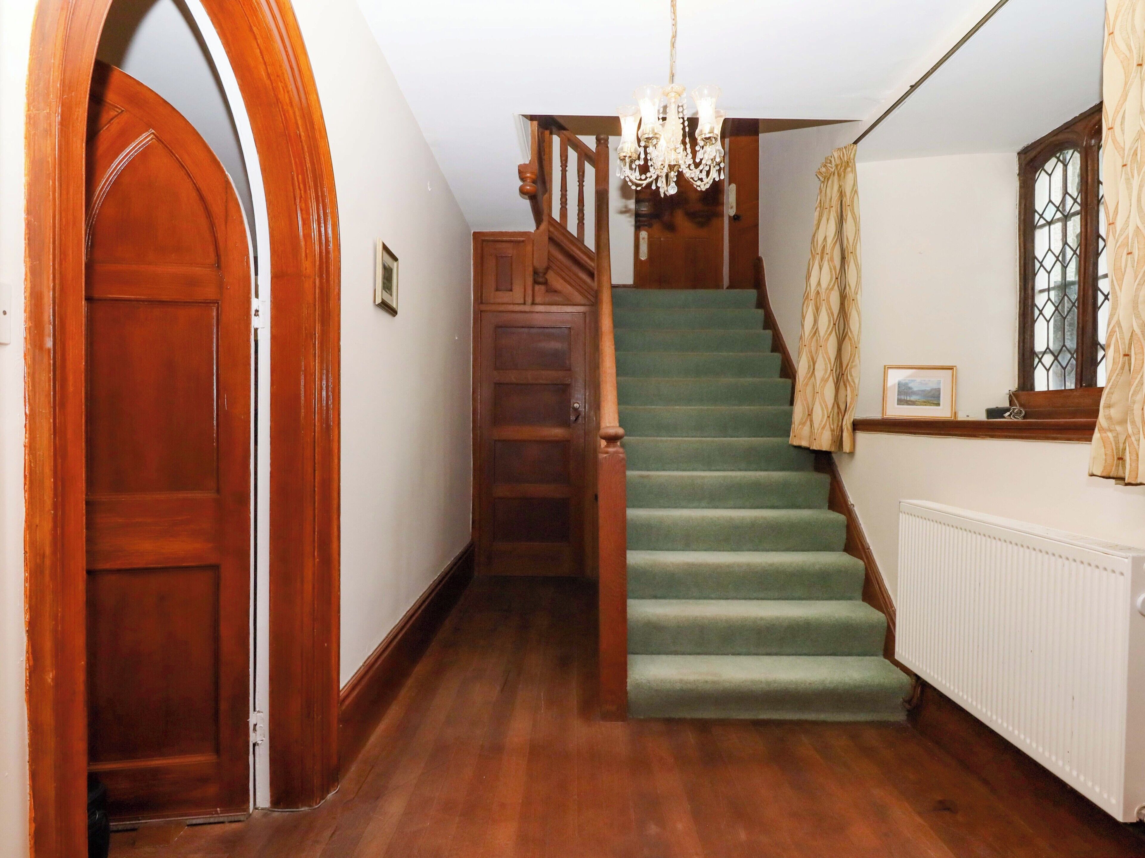 A staircase with green carpet, wooden handrails, and a chandelier.