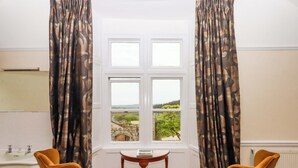 Une pièce avec vue sur un paysage, un lavabo blanc, deux chaises et une petite table.