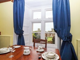 Mesa puesta con platos, una jarrón y copas de vino, con vista a un castillo a través de una ventana.