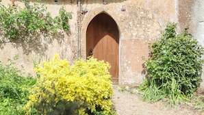 A rustic building with a wooden door, a brick chimney, and surrounding greenery. - Dowrich West Wing Apartment (Crediton)