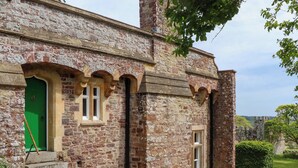 Un bâtiment en pierre avec une porte verte, des fenêtres en arc de cercle et une cheminée en briques.