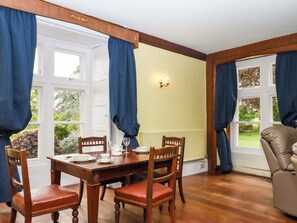 Un comedor con una mesa y sillas de madera, una ventana con cortinas, y una lámpara fijada a la pared.