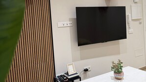 Moderni olohuone, jossa seinälle on asennettu taulutelevisio, seinässä on puulistapaneeli, huoneessa on pöytä, jossa on ruukkukasvi, sekä pieni sivupöytä, jonka päällä on kehystetty esine.