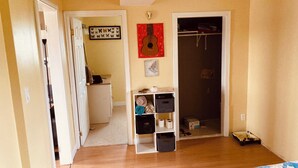 Una habitación con cama, armario, estante con cajas de almacenamiento y puerta que da a otra estancia.