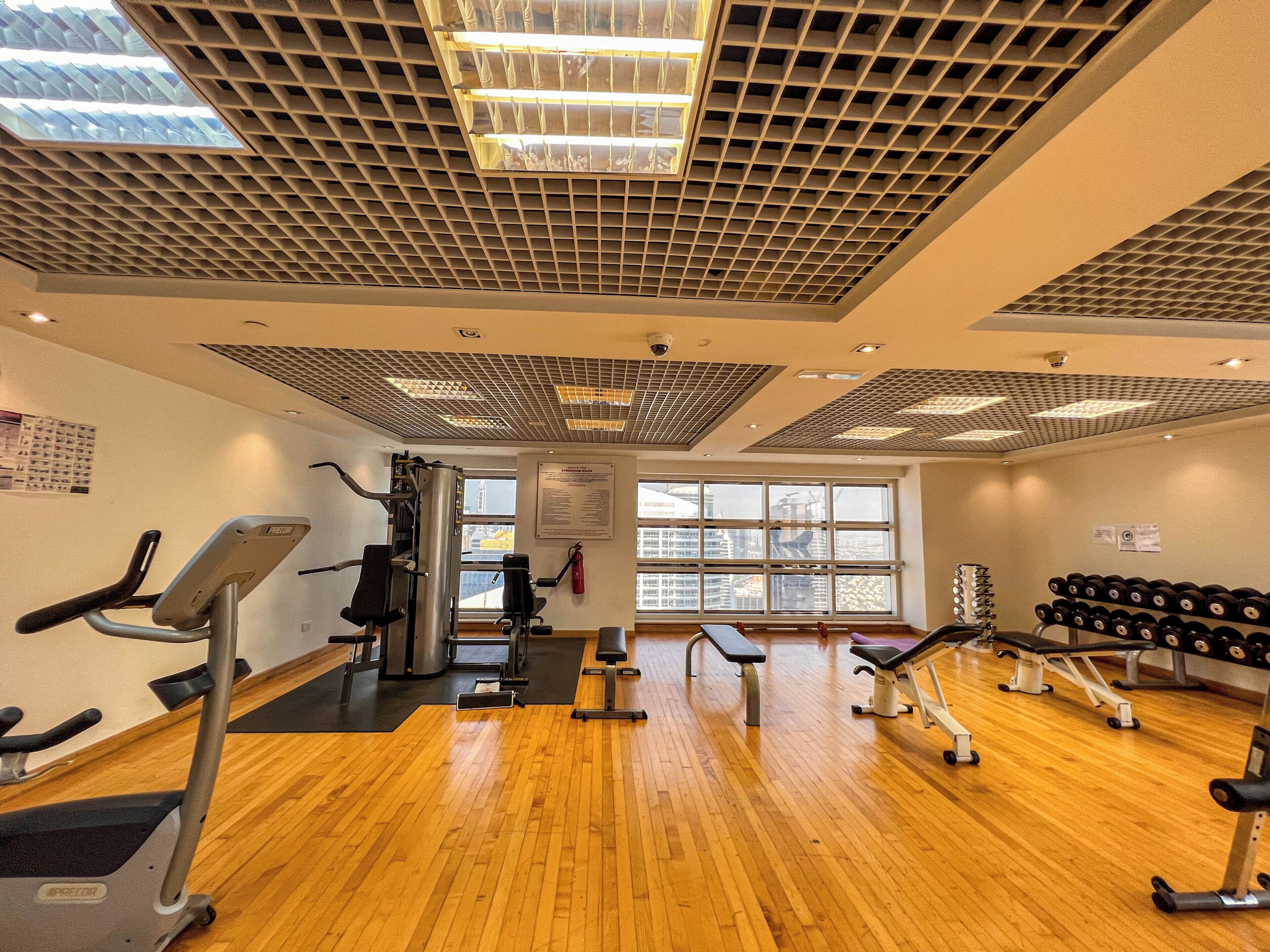 Ein Fitnessraum mit Trainingsgeräten, Holzboden und großen Fenstern.