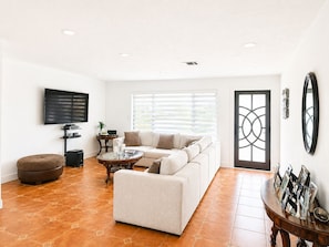 Ein Wohnzimmer mit Sofa, Hocker, Couchtisch, Fernseher und einer Tür mit geometrischem Muster.