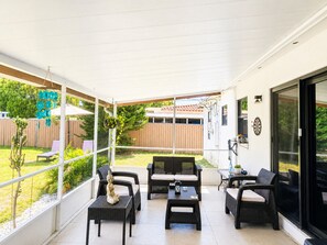 Eine überdachte Terrasse mit Korbmöbeln, einer Buddha-Statue und Blick auf einen Garten.