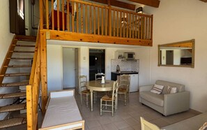 Eine zweistöckige Wohnung mit einer Holztreppe, einem Essbereich mit Tisch und Stühlen, einer Küche mit Mikrowelle und einem Sofa.