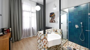 Un baño moderno con ducha, lavabo y espejo. Hay una ventana con cortinas y un cuadro en la pared.
