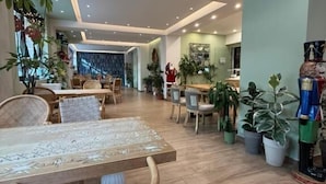 Un comedor amplio con una mesa y sillas de madera, rodeado de plantas en macetas y un gran jarrón decorativo.