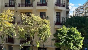 Un edificio residencial de varios pisos con balcones, ventanas y árboles en primer plano.