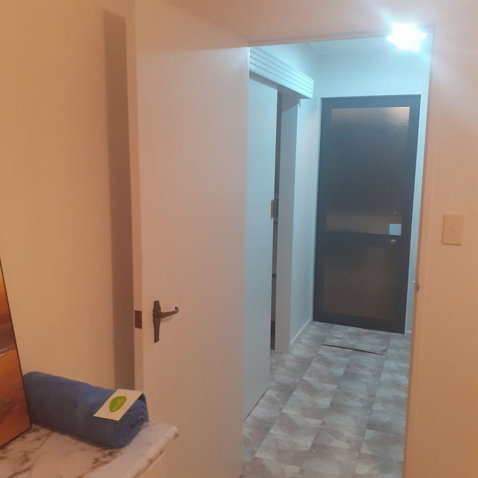 A hallway with a closed door at the end, a small bench with a towel, and a tiled floor.