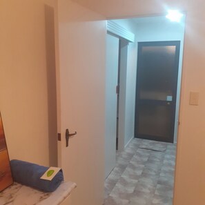 A hallway with a closed door at the end, a small bench with a towel, and a tiled floor. - Country Charm Cozy  Cottage - Meets NZ HH heating Cert. Outdoor Wood fired bath (Bunnythorpe)