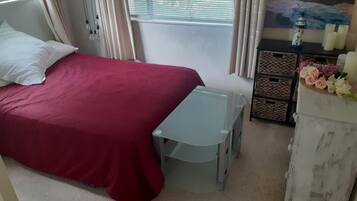 A bedroom with a bed, a small table, a dresser, and a window with curtains.