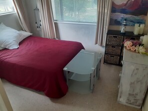 A bedroom with a bed, a small table, a dresser, and a window with curtains. - Country Charm Cozy  Cottage - Meets NZ HH heating Cert. Outdoor Wood fired bath (Bunnythorpe)