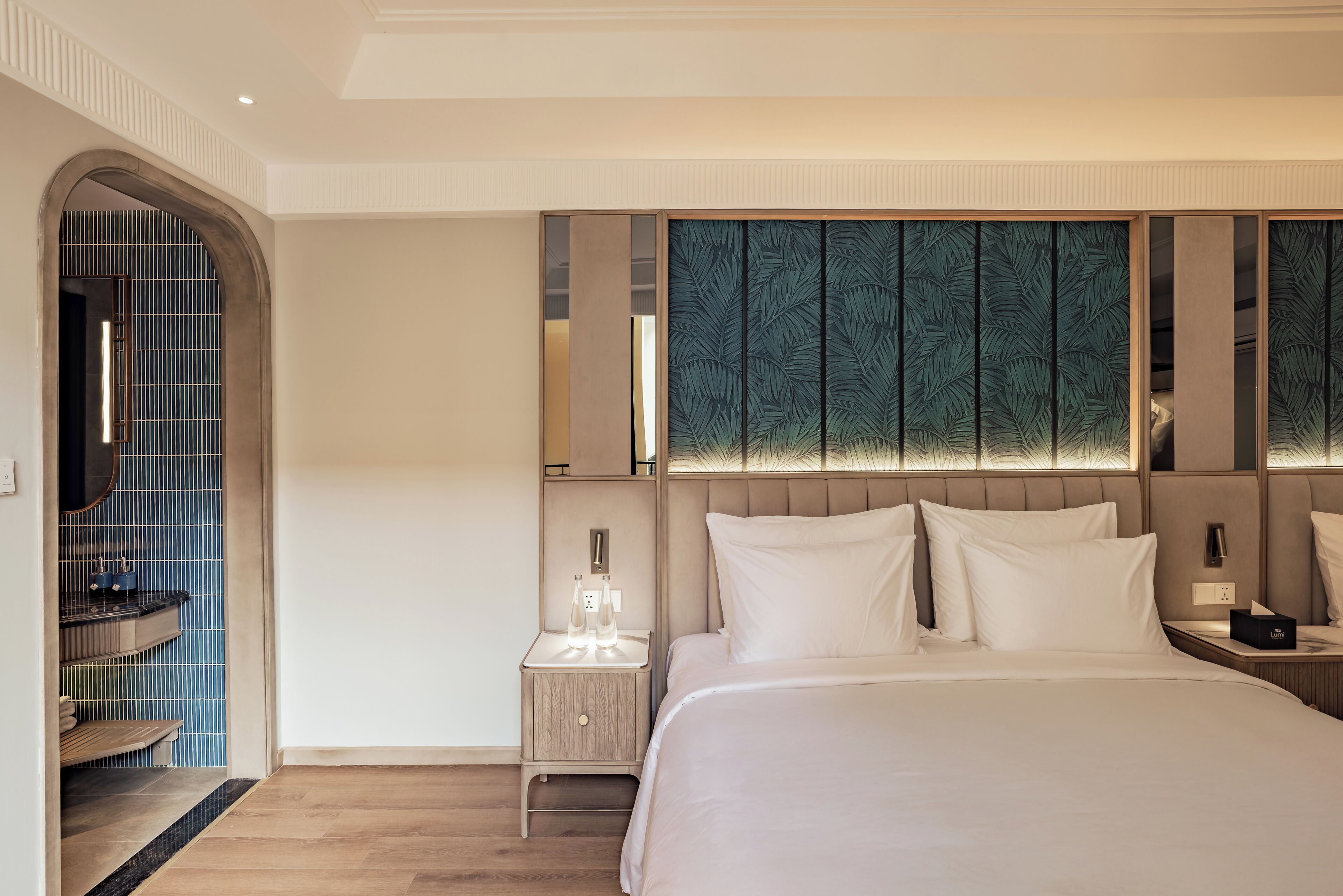 A modern hotel room with a large bed, a nightstand, a mirror, and a decorative wall panel.