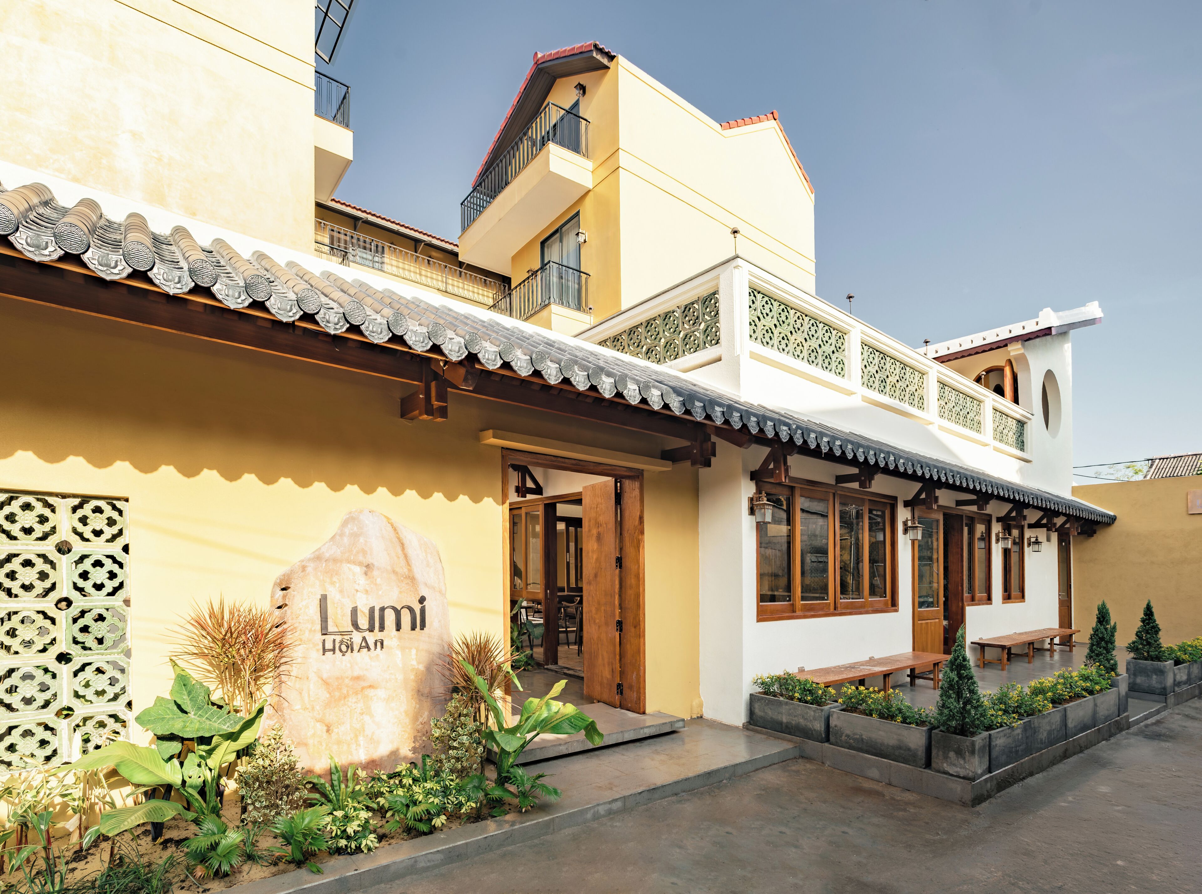 Un hotel de estilo arquitectónico tradicional, con una entrada destacada, zona de estar al aire libre y plantas decorativas.