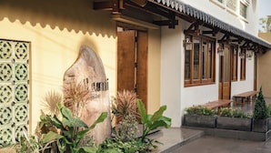 A building entrance with a wooden door, a large sign, and a small garden area with plants and a bench. - Lumi Hoi An Hotel (Da Nang)