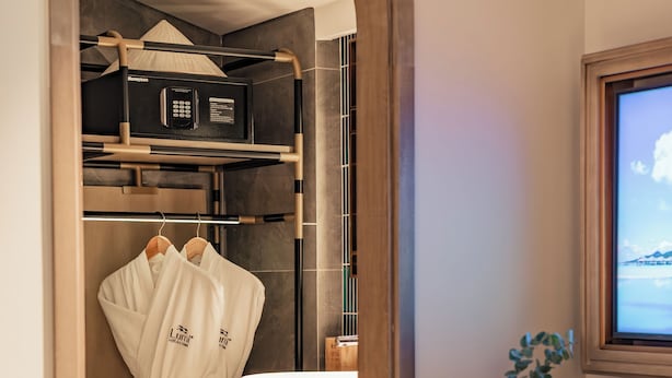 A hotel room with a walk-in closet, a bed, a desk with a chair, a sink, and a large window. - Lumi Hoi An Hotel (Da Nang)