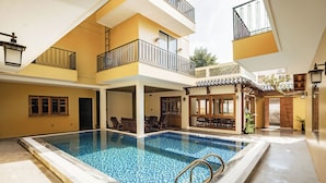 A swimming pool with a tiled deck, a covered seating area, and a two-story building with balconies. - Lumi Hoi An Hotel (Da Nang)