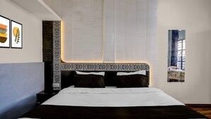 A neatly arranged hotel room with a large bed, a nightstand, a wall-mounted artwork, and a window with a view. - Deluxe Jalukbari Bus Stand Velvet Stay (Guwahati)