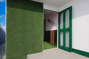 Entrada de un edificio moderno con una puerta verde, piso de concreto y una pared con diseño circular.