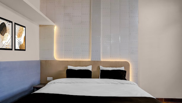 A modern hotel room with a large bed, a nightstand, and wall-mounted artwork. - Deluxe Jalukbari Bus Stand Velvet Stay (Guwahati)