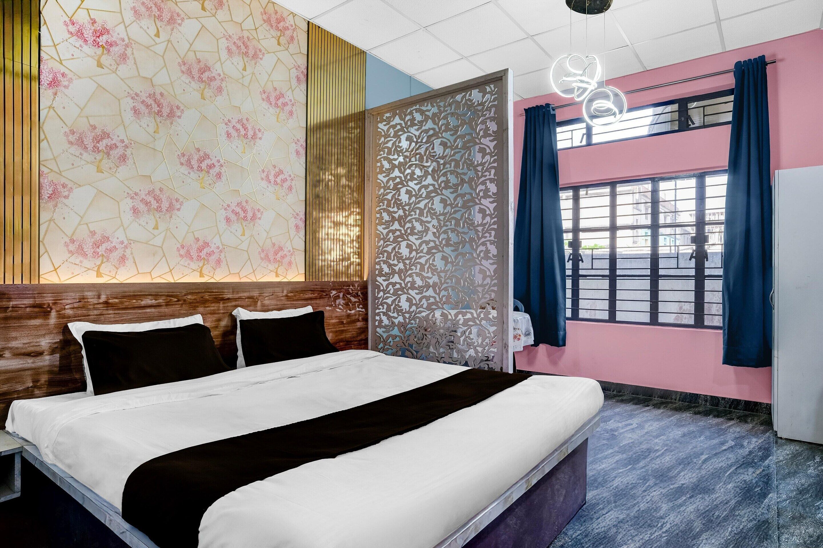 Una habitación de hotel con cama, un detalle decorativo en la pared, una ventana con cortinas y una lámpara en el techo.
