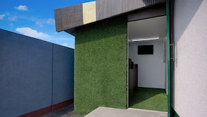 A modern building with a green artificial grass wall, a concrete floor, and a metal door. - Deluxe Jalukbari Bus Stand Velvet Stay (Guwahati)