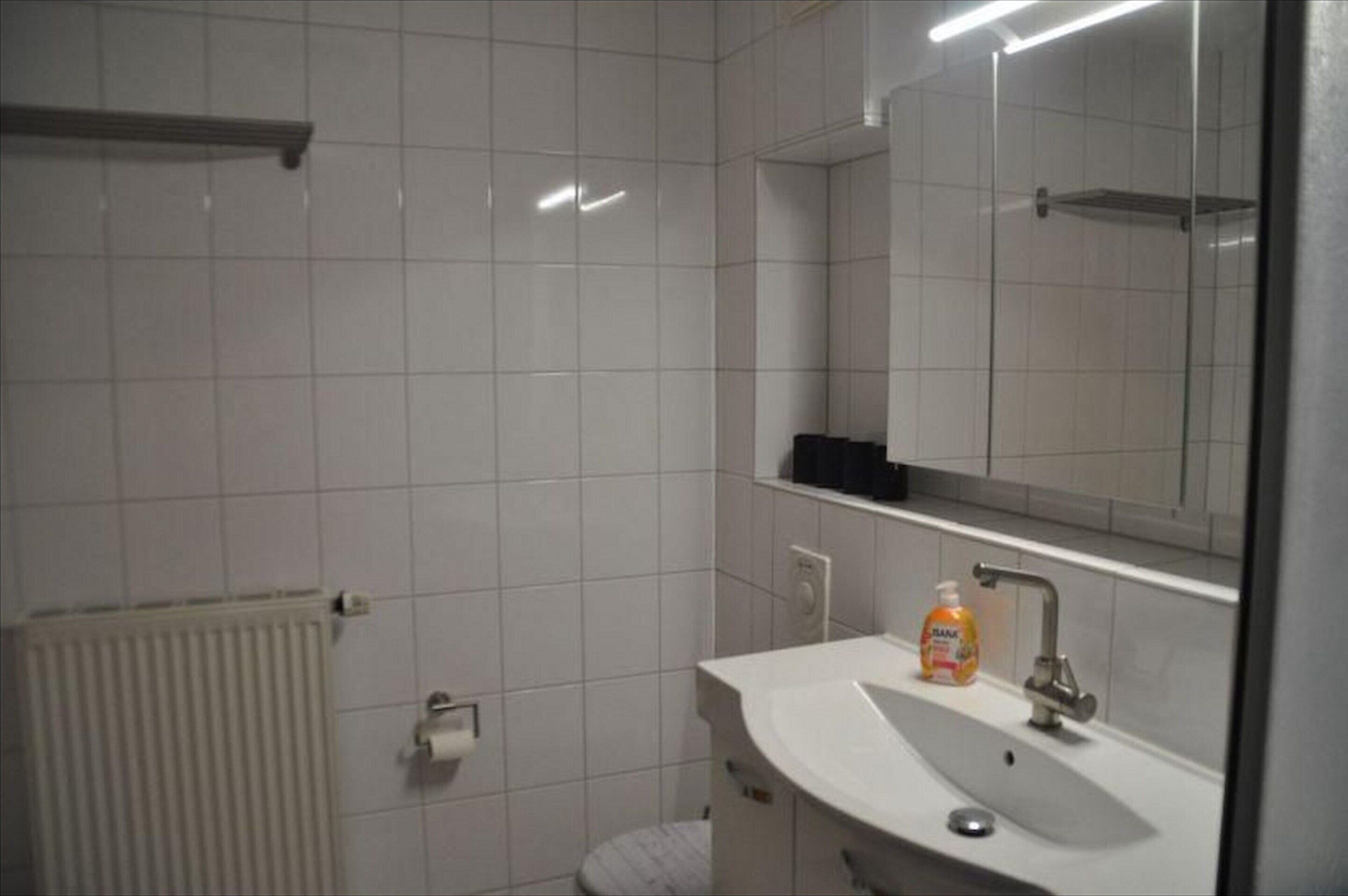 Kylpyhuone, jossa on valkoiset laatat, pesuallas, peili ja wc-istuin.