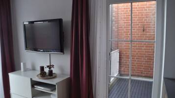 A room with a TV on a white cabinet, a window with red curtains, and a view of a brick wall outside.