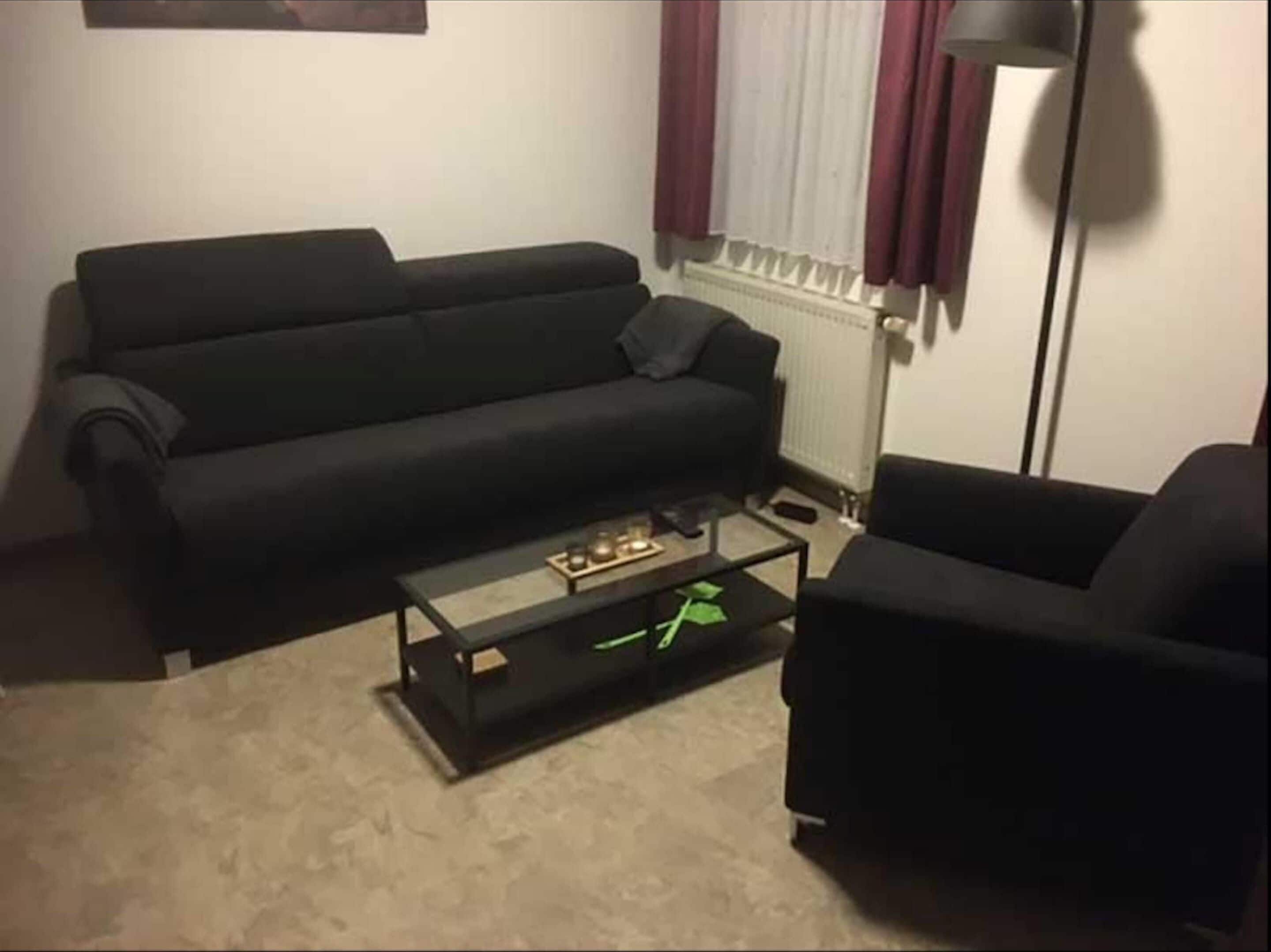 En stue med en sort sofa, et sofabord og en lampe.