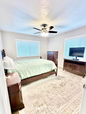 A bedroom with a bed, dresser, TV, and ceiling fan.