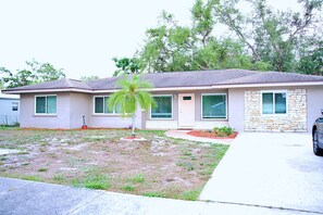 A single-story house with a stone facade, a front porch, and a small lawn with a palm tree.