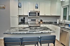 A kitchen with white cabinets, a marble countertop, a built-in oven, a microwave, and a sink.