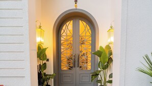A double door with a decorative glass pattern, flanked by two wall-mounted lanterns, and potted plants on either side. - ELIVAAS Purple Coral Luxe 5-BHK Villa (Assagao)