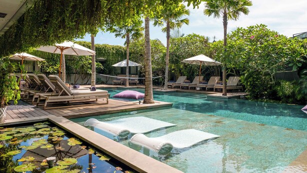 A pool area with lounge chairs, umbrellas, and a water feature with lily pads. - Luxury 9BR Bingin Villa - Large Pool, Near Beach (Kecamatan Kuta Selatan)