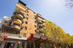 A multi-story building with balconies, a visible storefront, and a tree with yellow leaves. - Bright, quiet room with modern renovation and comfortable furnishings. (Yerevan)