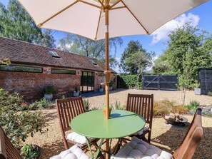 A patio with a table and chairs, a brick building, and a fenced area. - The Barn (Malvern)