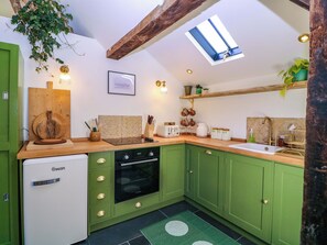 A compact kitchen with green cabinets, a built-in oven, a small refrigerator, and a window above the sink. - The Barn (Malvern)
