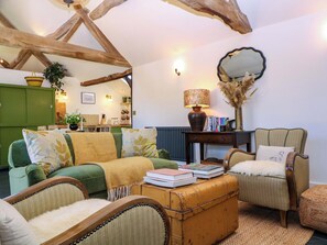 A cozy living room with a green sofa, a yellow armchair, a wooden coffee table with books, a lamp, and a mirror on the wall. - The Barn (Malvern)